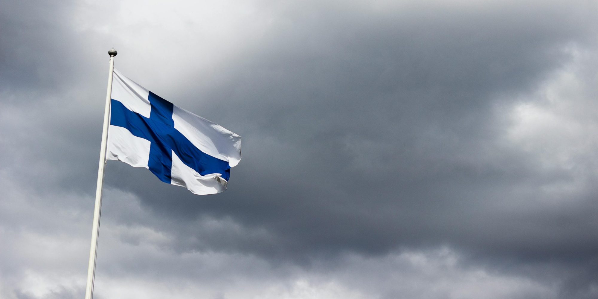 The Finnish flag waves proudly against a dramatic, cloudy sky, symbolizing national identity.